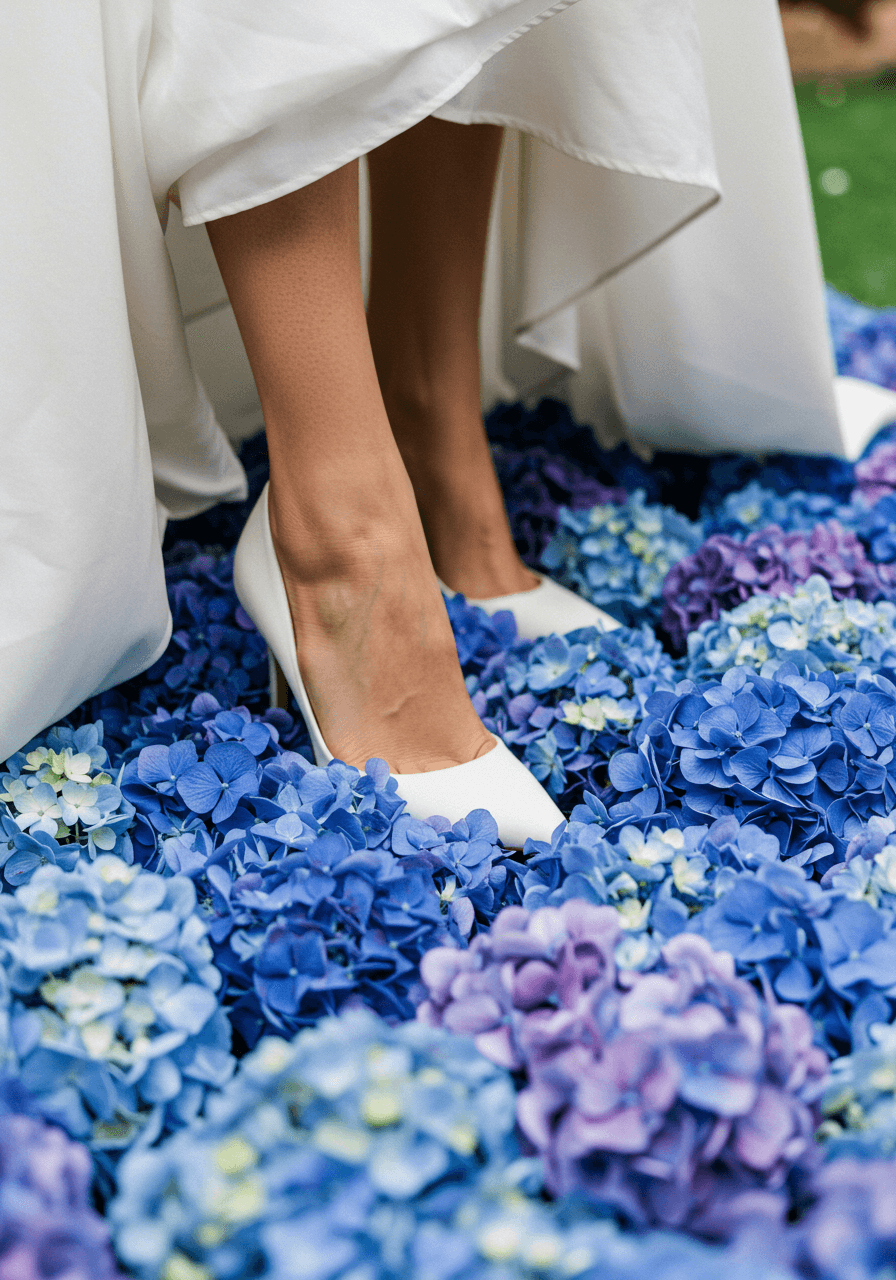 Close-up detail of bride's white satin shoes walking on blue hydrangea bloom carpet
