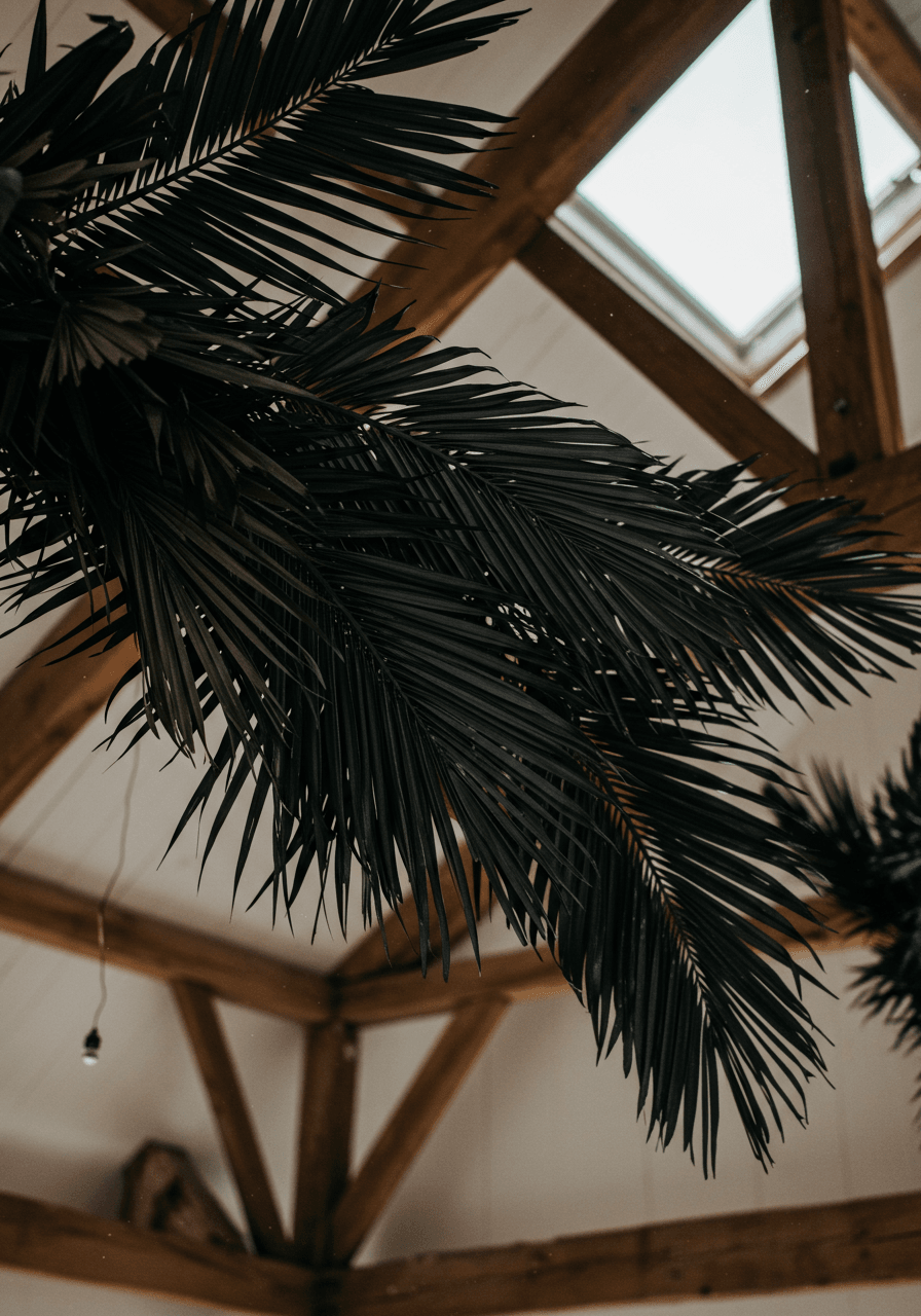 Large dried palm fronds spray-painted charcoal hanging from rustic wooden ceiling beams in converted barn